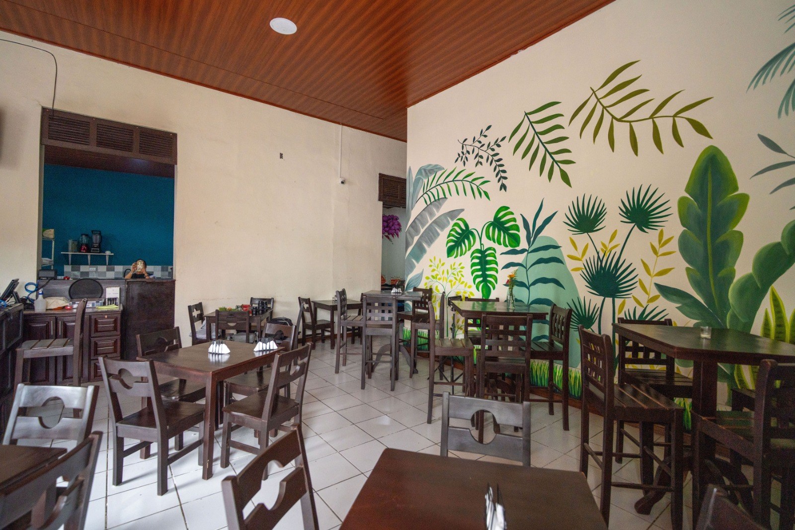 Interior de La Esquina Nica, con mesas y un mural de hojas tropicales